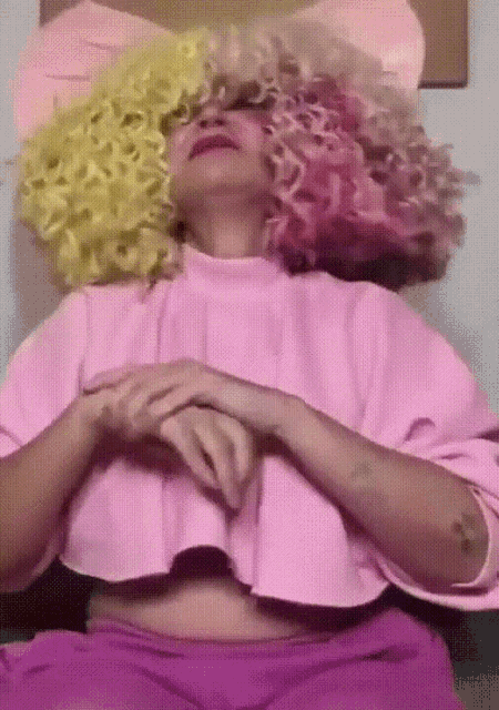 a woman wearing a pink crop top and pink pants has two wigs on
