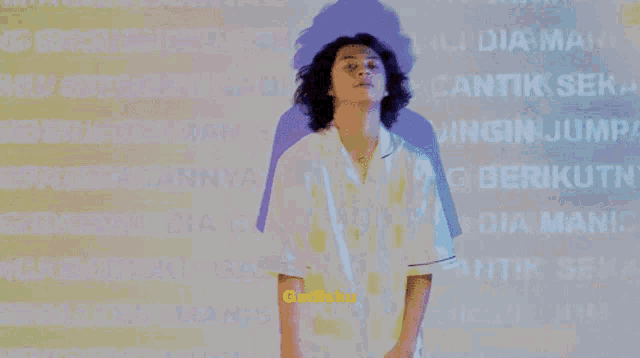 a man in a white shirt is standing in front of a wall that says " gadisku " on it