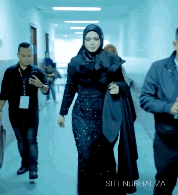a woman in a black dress is walking down a hallway with the name siti nurhaliza on the bottom right