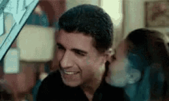 a woman is kissing a man on the cheek while they are smiling .