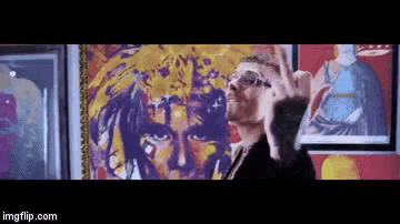 a man with glasses is standing in front of a painting of a woman 's face