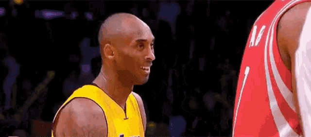 a basketball player wearing a yellow jersey is talking to another player wearing a red jersey .