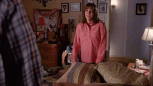 a woman in a pink shirt is standing next to a bed in a bedroom .