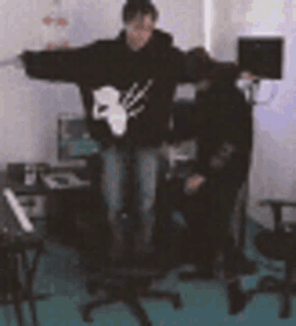 a man is standing in a room with his arms outstretched and a woman is sitting in a chair .