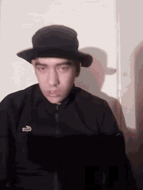a man wearing a hat and a black jacket with a lacoste logo
