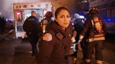 a woman in a firefighter uniform is standing in front of an ambulance at night .