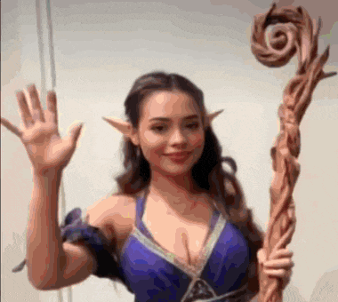 a woman in a blue dress with elf ears is holding a wooden cane and waving .