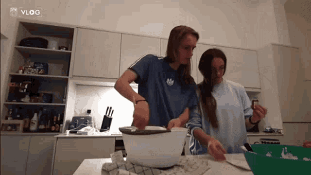 two women cooking in a kitchen with a vlog logo on the corner