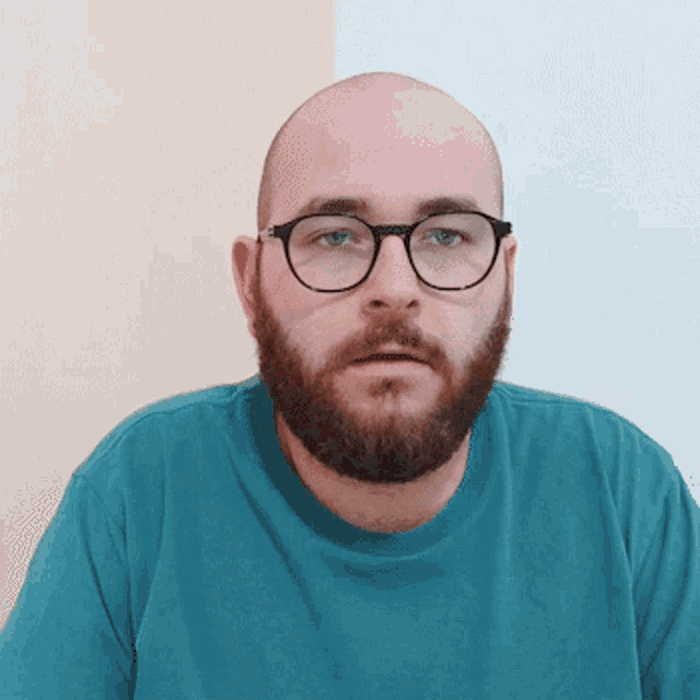 a bald man with glasses and a beard wears a blue shirt