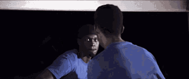 a man in a blue shirt looks at himself in a mirror
