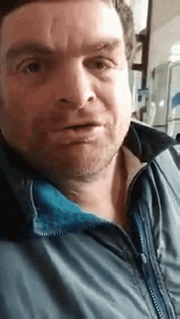 a man is wearing a blue jacket and making a funny face .