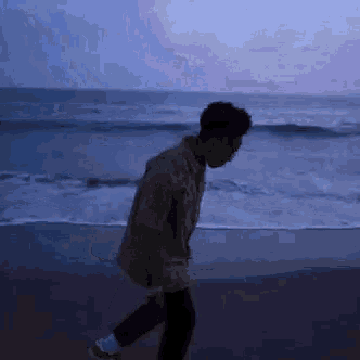 a man is walking on a beach near the ocean at night .