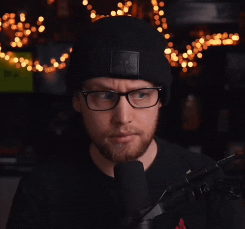 a man wearing glasses and a black beanie is speaking into a microphone