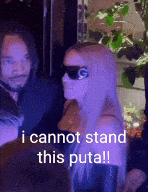 a woman wearing sunglasses is standing next to a man and says " i cannot stand this puta "