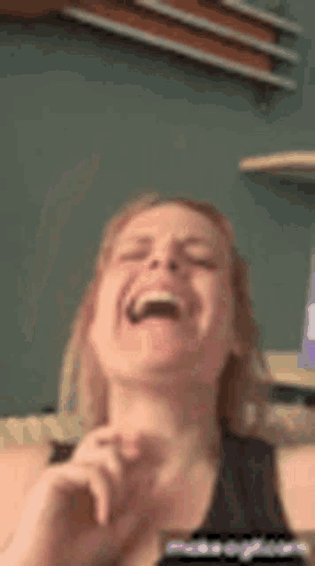 a woman is laughing with her mouth open in front of a blackboard .