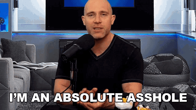 a bald man sitting in front of a microphone with the words i 'm an absolute asshole above him