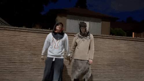 a man and a woman are standing next to each other holding hands in front of a brick wall .