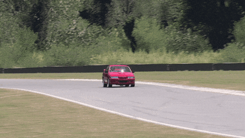a red car is driving down a road with trees in the background