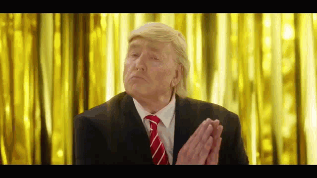 a man in a suit and tie is clapping his hands in front of a yellow curtain