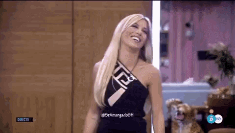 a blonde woman in a black dress is laughing in front of a dog .