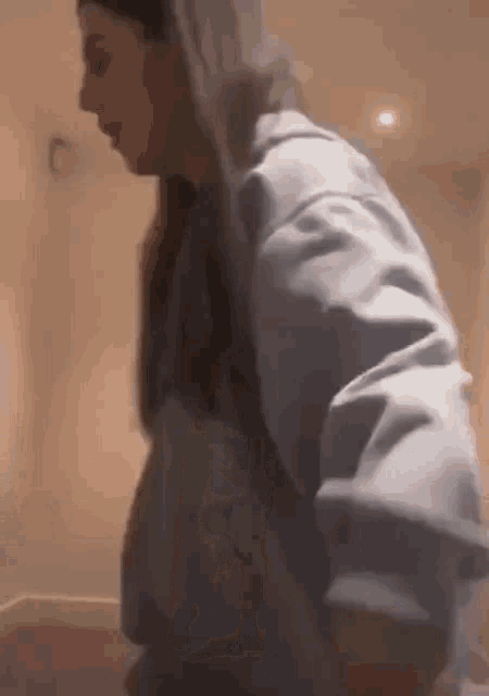 a woman in a blue hoodie is standing in a room and looking down .
