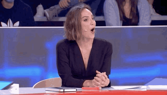 a woman in a black dress is sitting at a table with her mouth open
