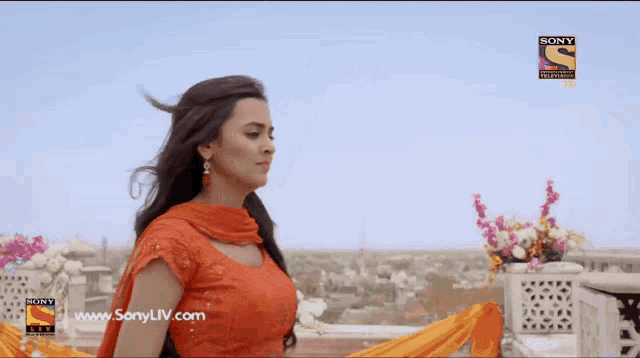 a woman in an orange dress stands in front of a sony television logo