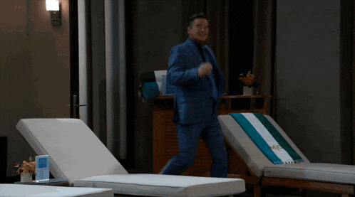 a man in a blue suit is dancing in a room with lounge chairs and a towel that says mc