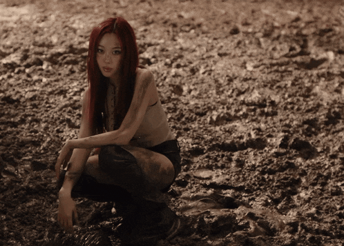 a woman with red hair is kneeling in a muddy field