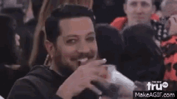 a man with a beard and mustache is sitting in a crowd of people and smiling .
