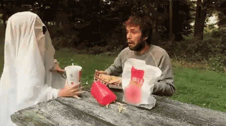 a man and a ghost are sitting at a picnic table .
