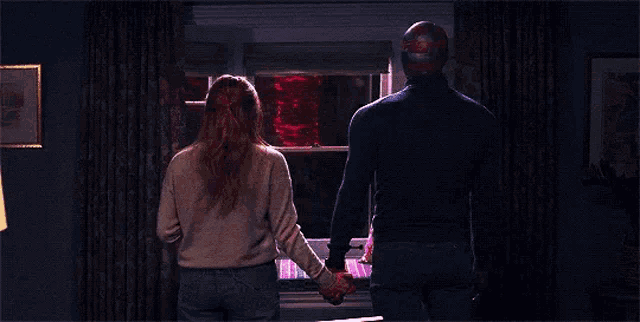 a man and a woman are holding hands while looking out a window .