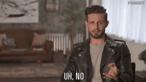 a man in a leather jacket is sitting in a chair in a living room and making a funny face .