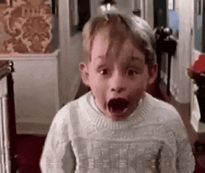 a young boy in a white sweater is making a surprised face in a hallway .