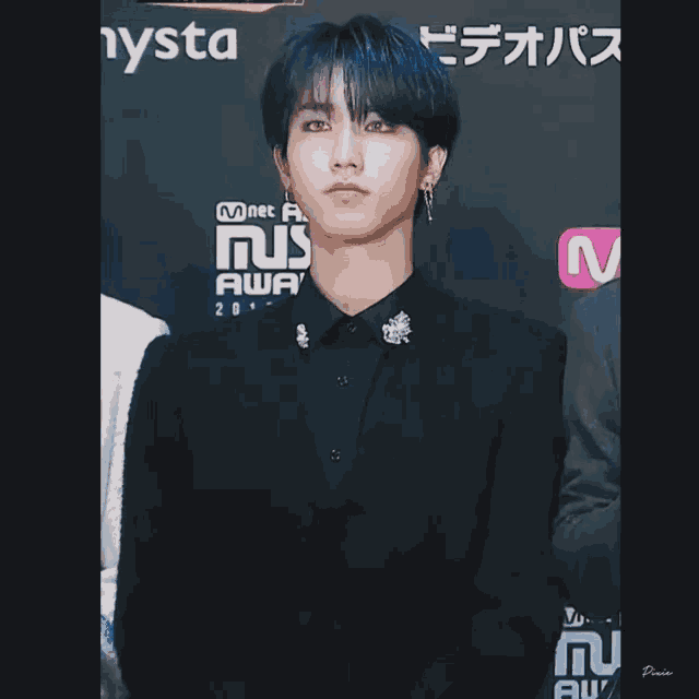 a young man in a black suit stands in front of a mnet music awards sign