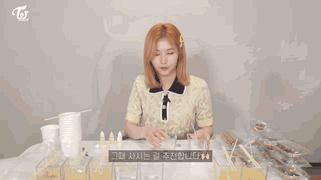 a woman sitting at a table with a twice logo on the bottom