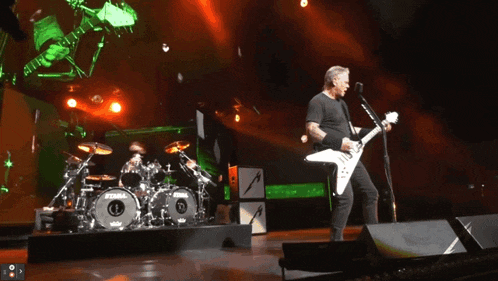 a man singing into a microphone while playing a guitar in front of a drum set