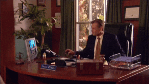 a man sits at a desk with a name plate that says dean rivers on it