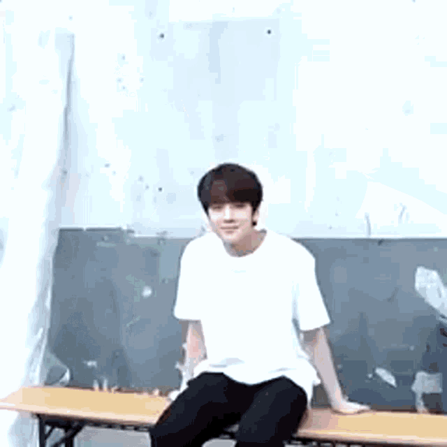 a man in a white shirt is sitting on a wooden bench .