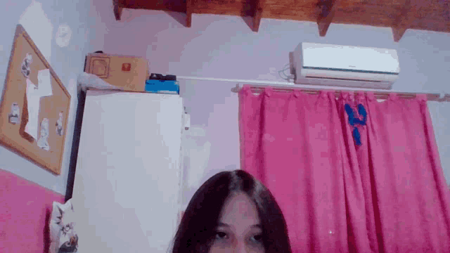 a girl stands in a room with pink curtains and a white refrigerator