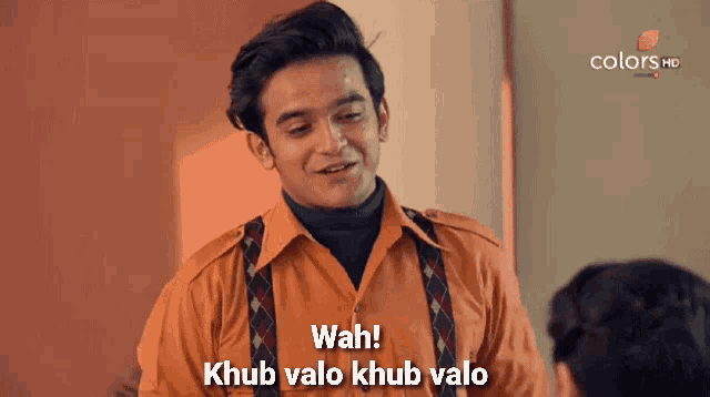 a man in an orange shirt is talking to another man and says wah !