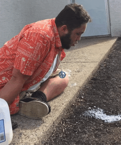 a man in a red shirt sits on the sidewalk next to a milk carton