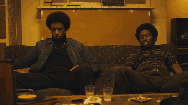 two men sitting on a couch with a record player in the background