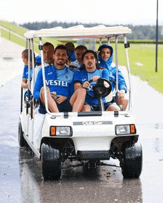 a group of soccer players are riding in a golf cart on a wet road .