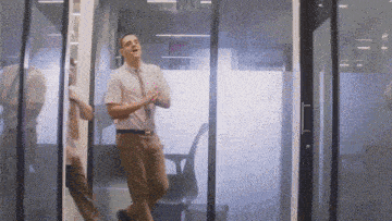 a man in a pink shirt and tie stands in front of a glass door that says exit on it