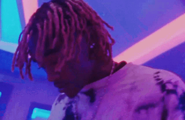 a man with dreadlocks is standing in front of a microphone in a room with purple lights .