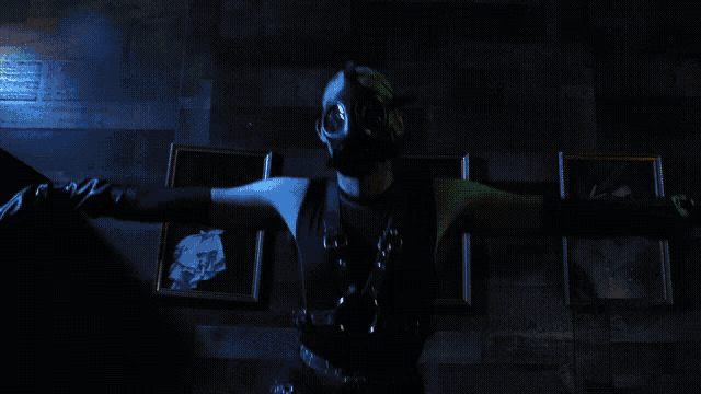 a man wearing a gas mask and leather gloves stands in a dark room
