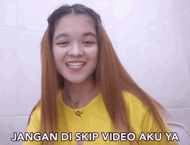 a woman in a yellow shirt is smiling with the words jangan di skip video aku ya below her