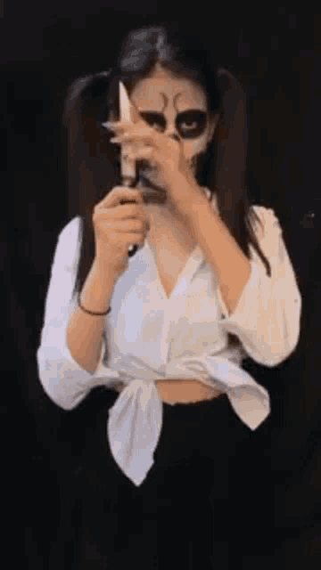 a woman with makeup on her face is holding a knife in her hand .