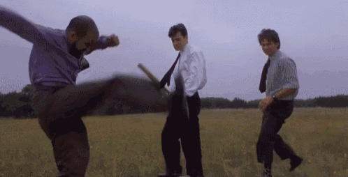 a man is kicking a stick in a field while another man watches .